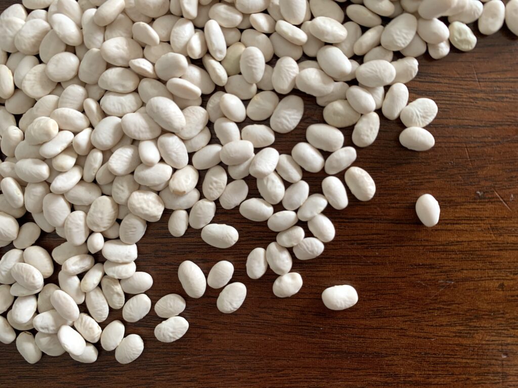 A pile of small, white dried beans spills out over a dark brown wooden table.