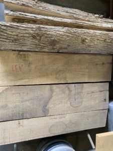 Quartersawn logs stacked up, with measurements and markings penciled on them in red