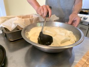 Close up of Minh scooping soft tofu from the mixing bowl with a black ladle
