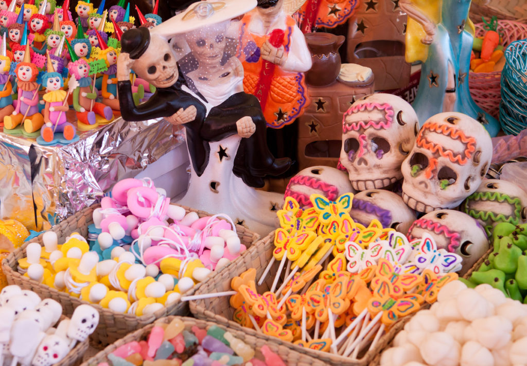 Brightly colored candies in the shape of clowns, butterflies, and skulls sit on a tabletop. Some of the clowns are holding signs that read "para mi amor."