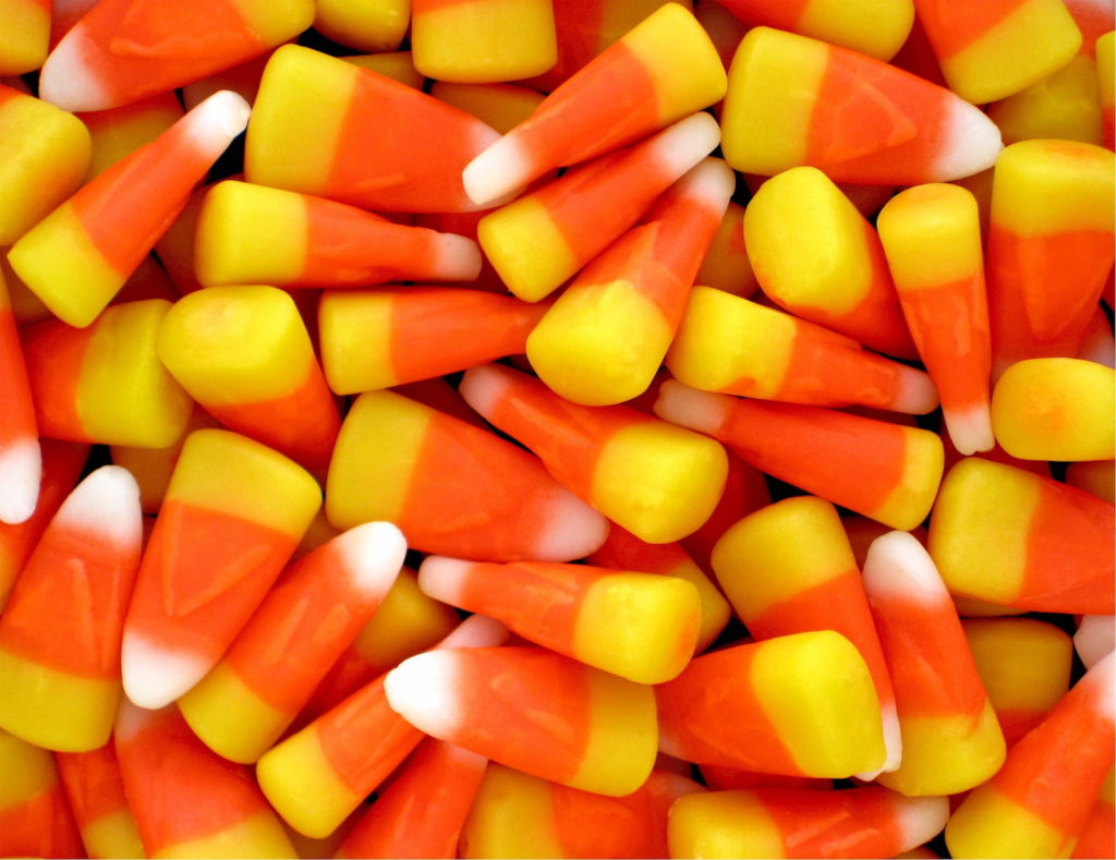 A close up overhead shot of several dozen pieces of candy corn, brightly colored in yellow, orange and white.