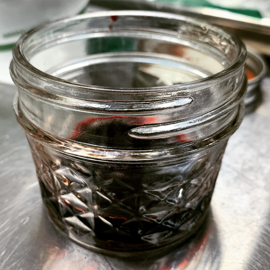 Close-up of a small glass jar containing a vermillion liquid