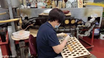 A repeating GIF of a woman in a blue shirt folding fortune cookies by bending disks over a metal dowel.