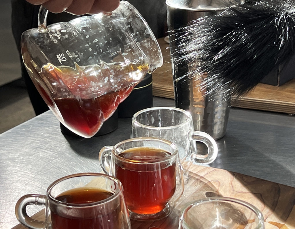 A feathery black microphone held out to a clear pitcher of coffee being poured into three clear glass mugs