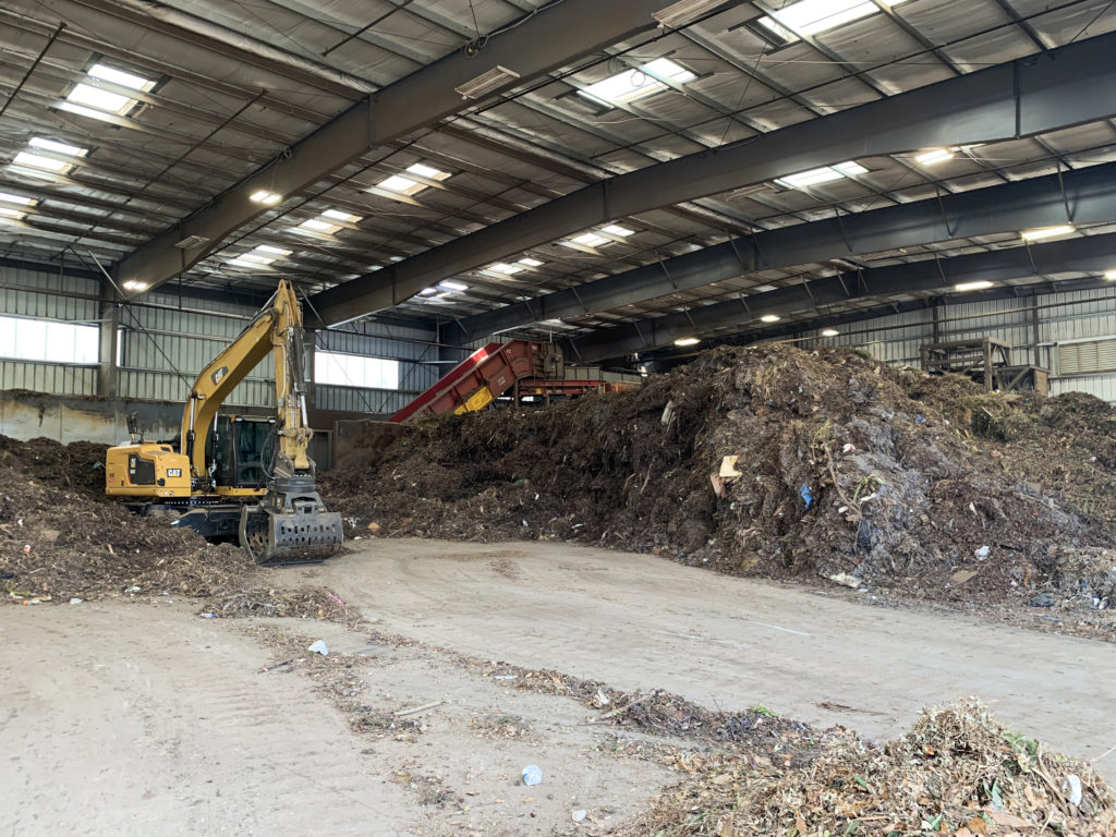A huge, room filled with piles of food waste and soil, being scooped up by yellow digger machines