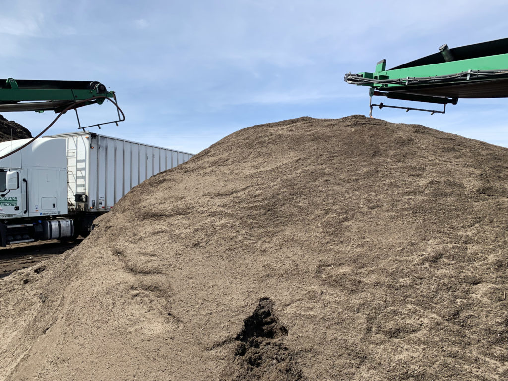 A pile of smooth gray-brown compost in front of a hazy blue sky