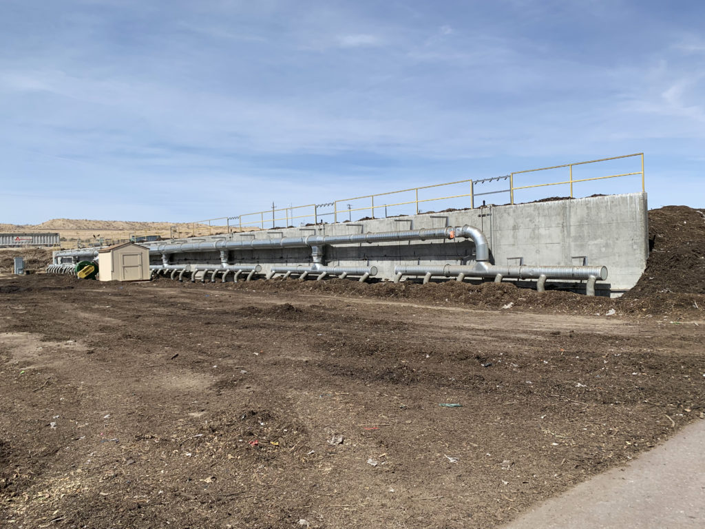A field of dirt with a concrete wall on the far end and metal ducts to blow air 