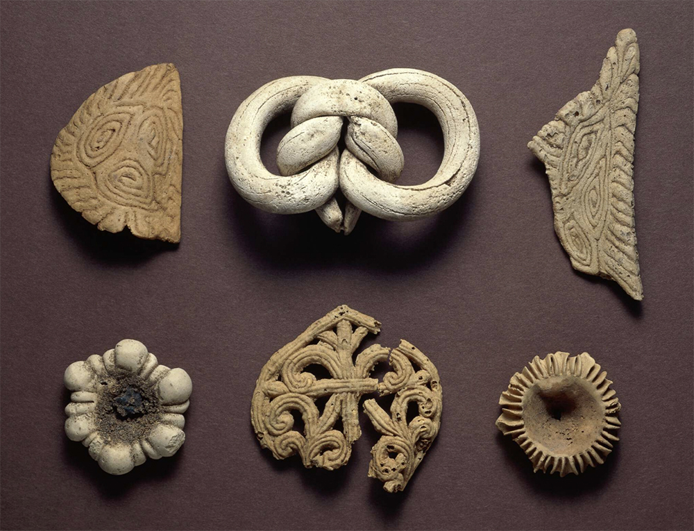 Six ancient cookies: a thin diamond wafer with swirling patterns; a pretzel-like treat; a wing-shaped wafer with swirls; two jam cookies with empty centers surrounded by ridges; and an elaborate, teardrop shaped cookie with scrollwork like the lattice of a gate, which is partially broken.